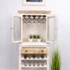 A white cabinet with wine glasses and plants on top of it.