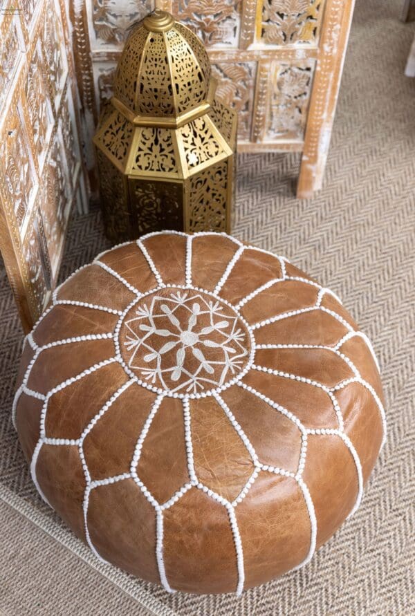 A brown leather ottoman with white stitching on the top.