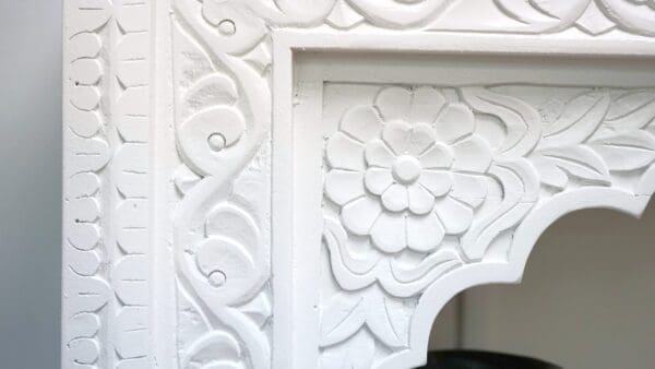 A white fireplace with floral design and ornate moldings.