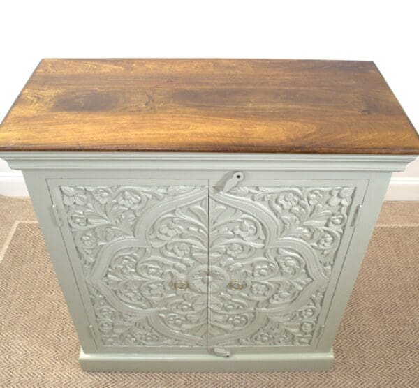 A white cabinet with wood top and carved design.