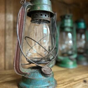 A green and blue vintage hurricane lantern sitting on top of a wooden table.