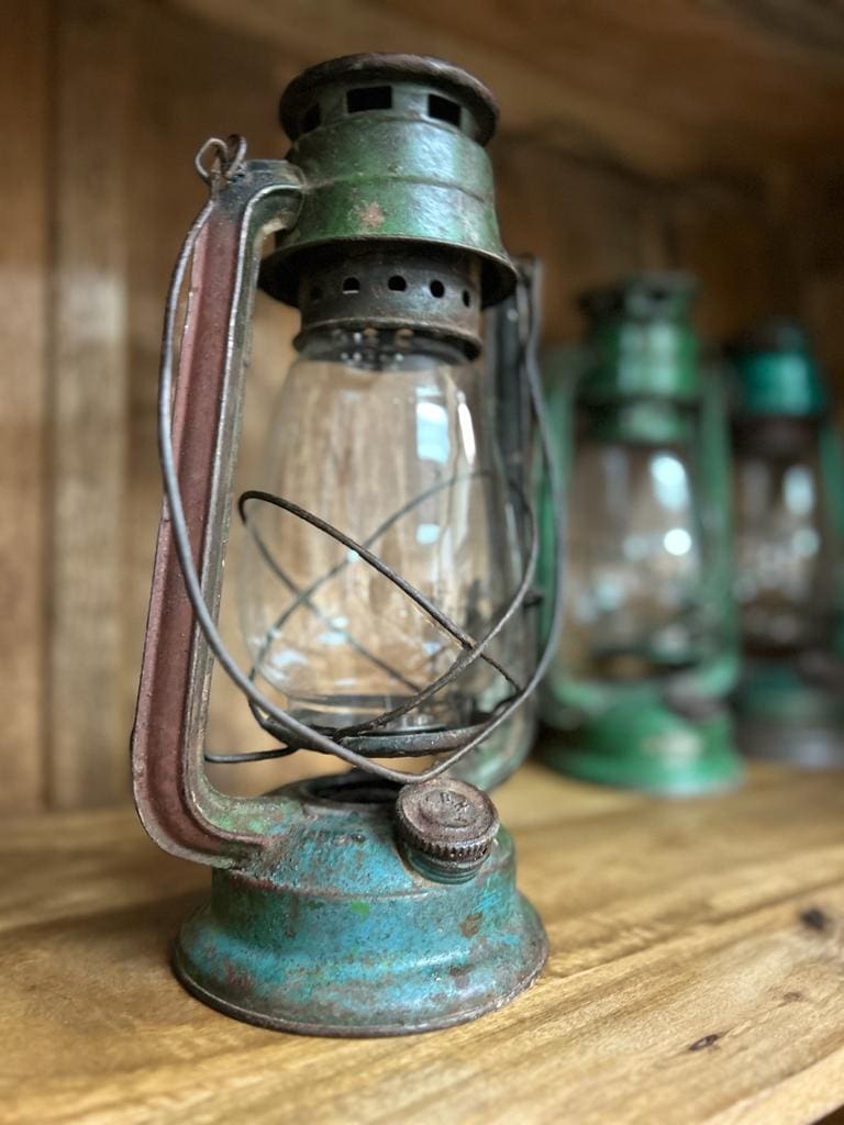 A green and blue vintage hurricane lantern sitting on top of a wooden table.