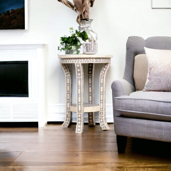 A living room with a couch and chair and a gray and white side table made of bone inlay.