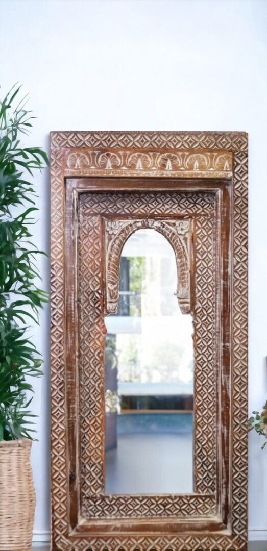 Large temple style mirror. Hand-crafted wooden beveled frame with hand carved detail and arched design, staged in a home next to a plant.