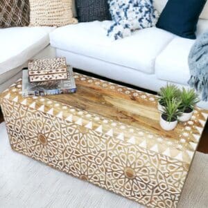 Hand-crafted natural wood coffee table made of mango wood with hand carved details in white, staged in a living room.