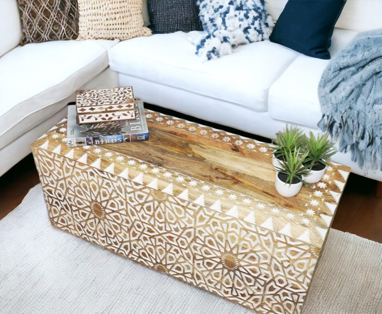 Hand-crafted natural wood coffee table made of mango wood with hand carved details in white, staged in a living room.