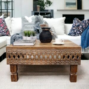 Hand-crafted natural wood square coffee table with hand-carved detail staged in a living room with decorative accents.