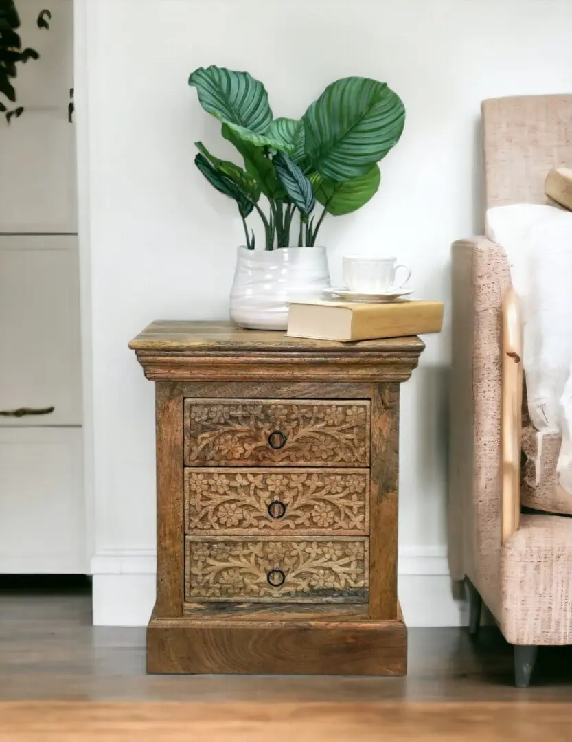 Natural wood nightstand with 3 drawers staged as an accent table in a living room with decorative accents.