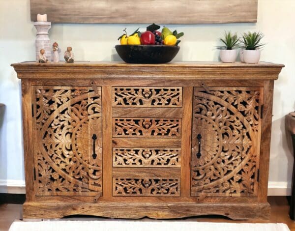 Stunning hand-carved solid natural wood sideboard with 2 carved doors and 3 carved drawers with an intricate cut out design staged in a home with decorative accents.