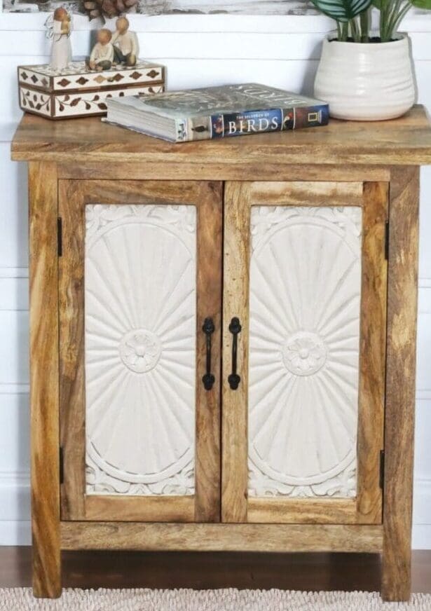 Natural wood cabinet with contrasting white carved doors with a sunburst design staged in a home with decorative accents.