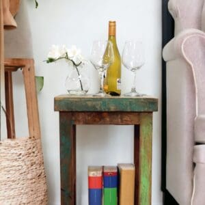 A reclaimed wood side table with decorative accents staged in a living room. Multicolored wood square tall table with a bottom shelf.