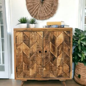 Hand-crafted wooden cabinet with two doors staged in a home with plants and decorative items. Herringbone cabinet, herringbone design on the doors of different pieces of wood,