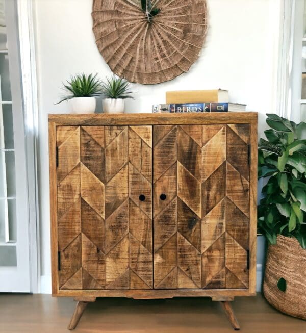 Hand-crafted wooden cabinet with two doors staged in a home with plants and decorative items. Herringbone cabinet, herringbone design on the doors of different pieces of wood,