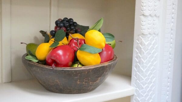 A bowl of fruit on top of a shelf.