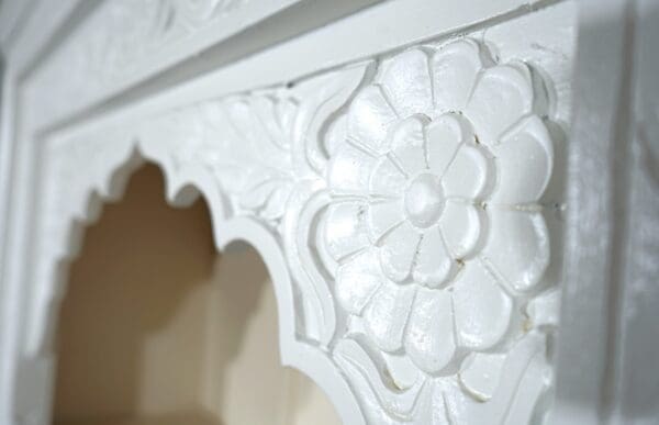 A white fireplace mantle with carved flowers on it.