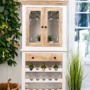 A white and wood cabinet with wine bottles on top of it.