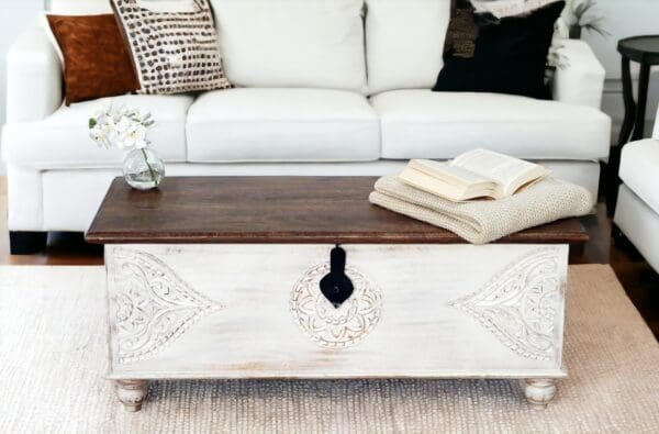 Hand-crafted solid wood white trunk with a dark top and hand-carved detailing. Staged in a living room.