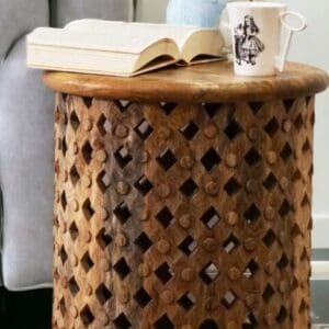 Natural wood lattice side table with a arm chair in the background staged in a living room