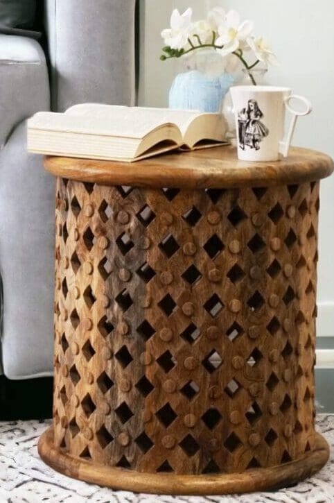 Natural wood lattice side table with a arm chair in the background staged in a living room