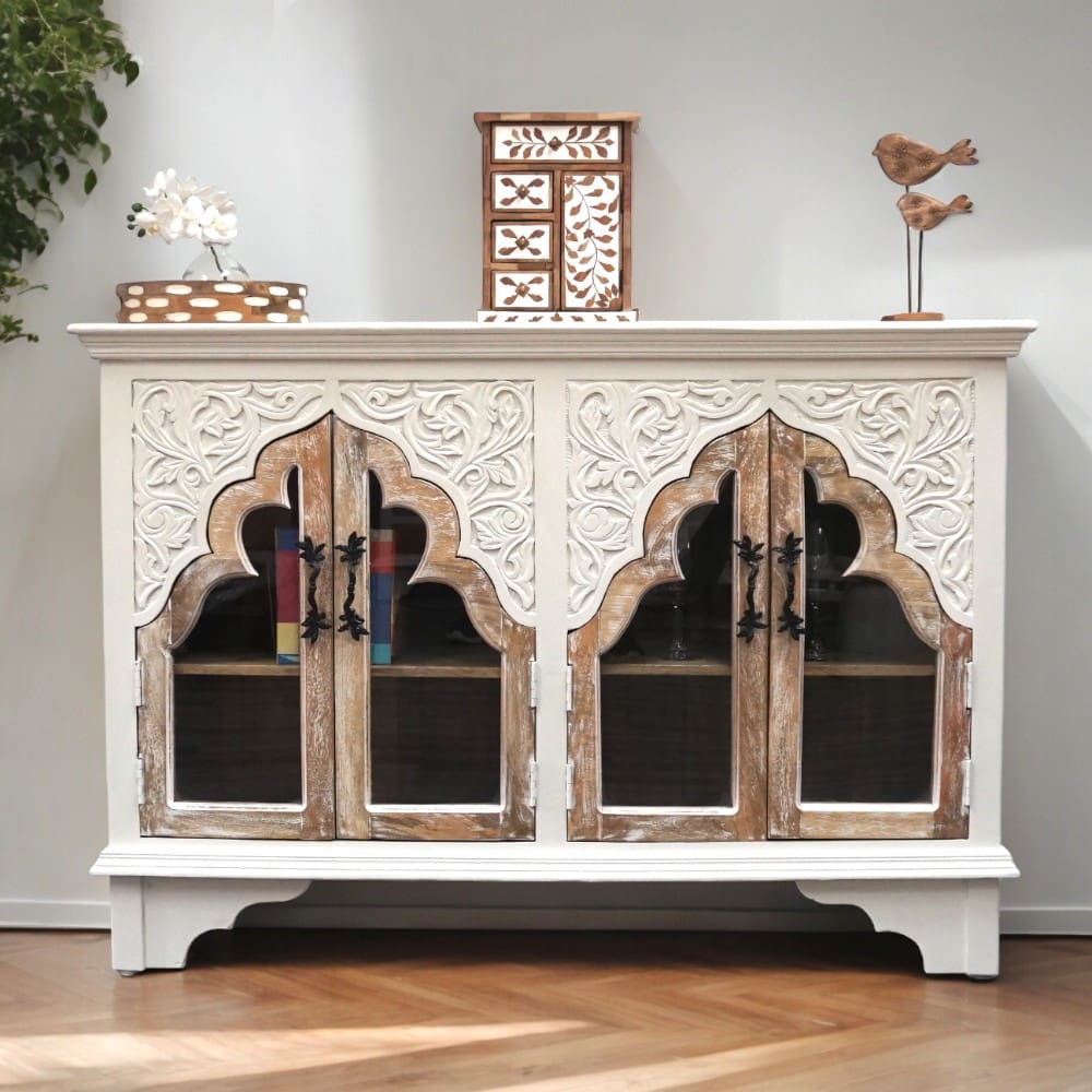 Hand-crafted solid wood arched sideboard. Four arched glass doors in natural wood, in a white sideboard woth hand-carved detailing staged in a home.