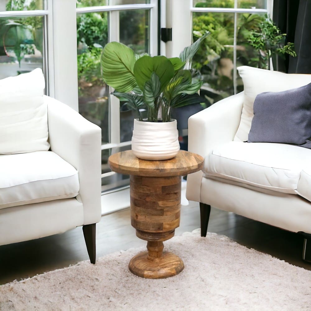 natural wood plant stand side table staged in a living room between two chairs