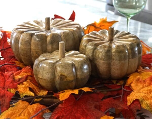 three hand-crafted wood fall pumpkins staged on a dining table.