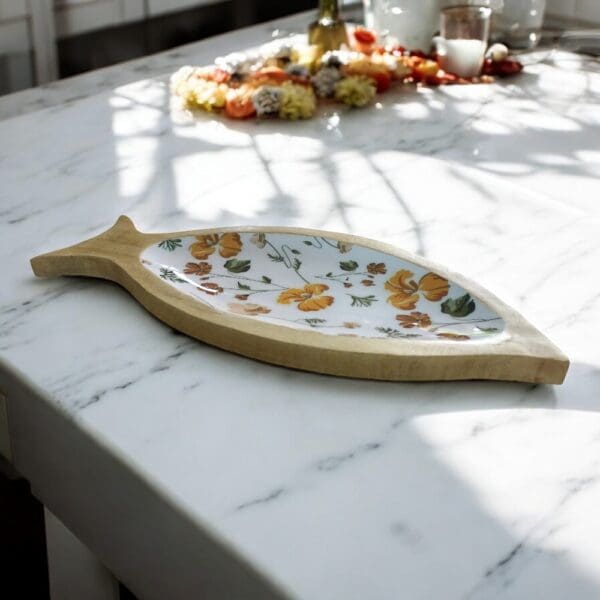 Hand-crafted shallow wooden fish dish with fall colored poppy flower enamel staged on a kitchen counter