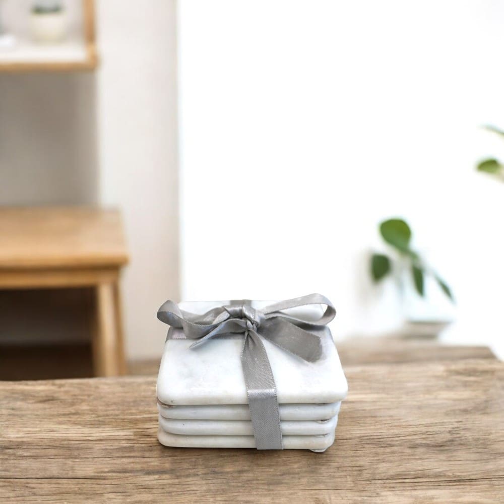 Set of 4 square marble coasters with rounded corners. Wrapped with a silver ribbon staged on a kitchen table.