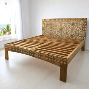 Hand-crafted solid wood, hand-carved king bedframe. Natural wood with white highlights staged in a sunny bedroom.
