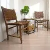 Pair of chairs. hand-crafted from solid mango wood with hand-woven brown leather lattice seat and backrest staged in a sunny home with a small table in between